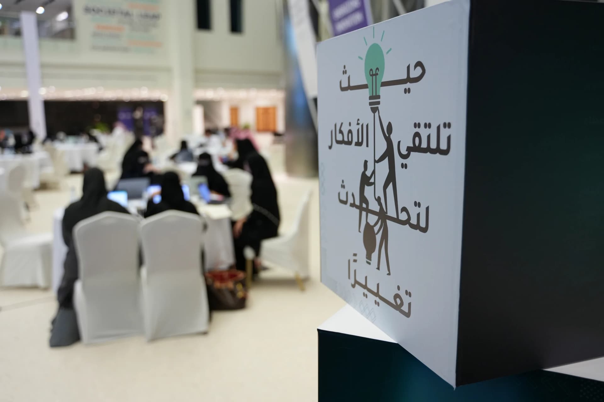 لوحة شعار قفاثون «حيث تلتقي الأفكار لتُحدث تغييرًا» وخلفها فرق تعمل